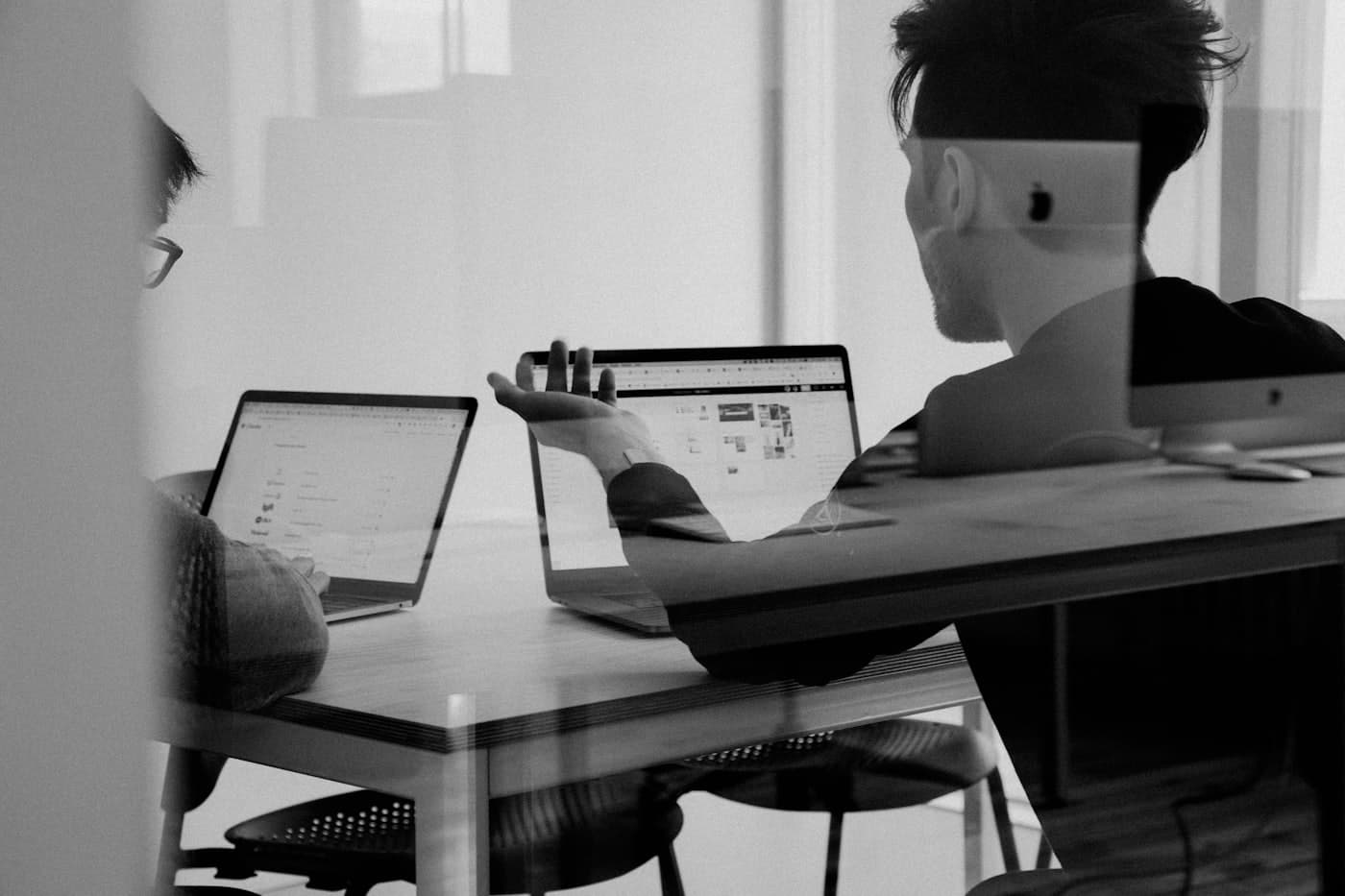 Two colleagues talking across laptops in a meeting room